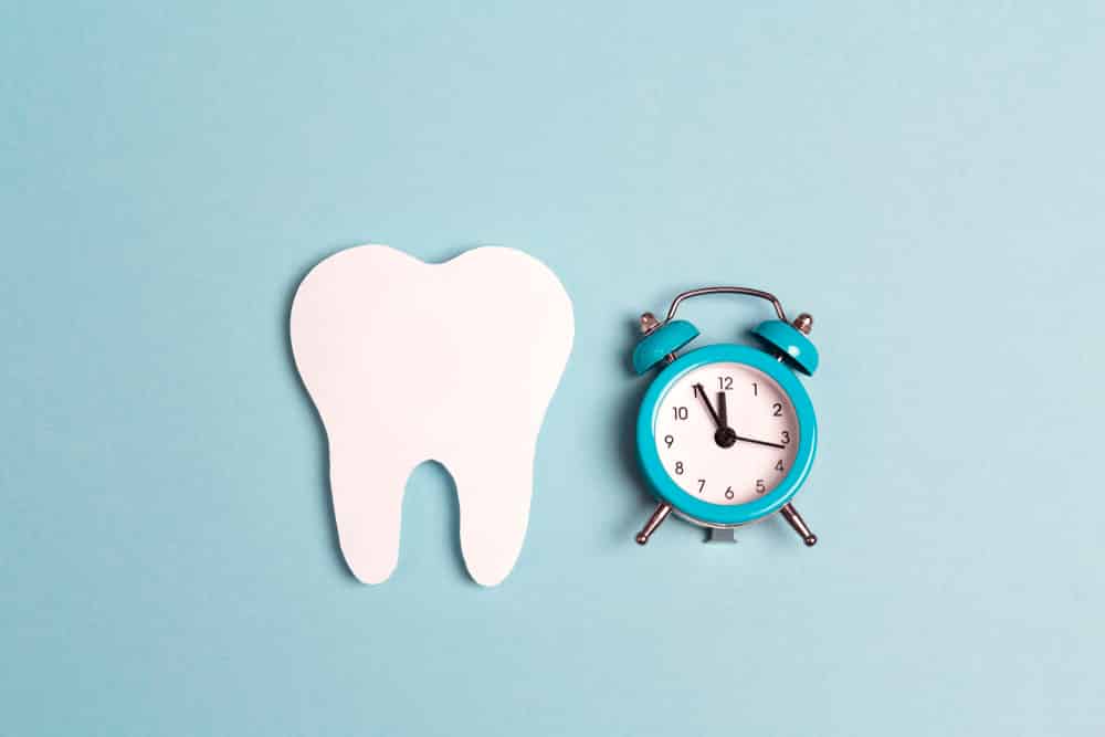 White paper tooth with alarm clock on blue background.