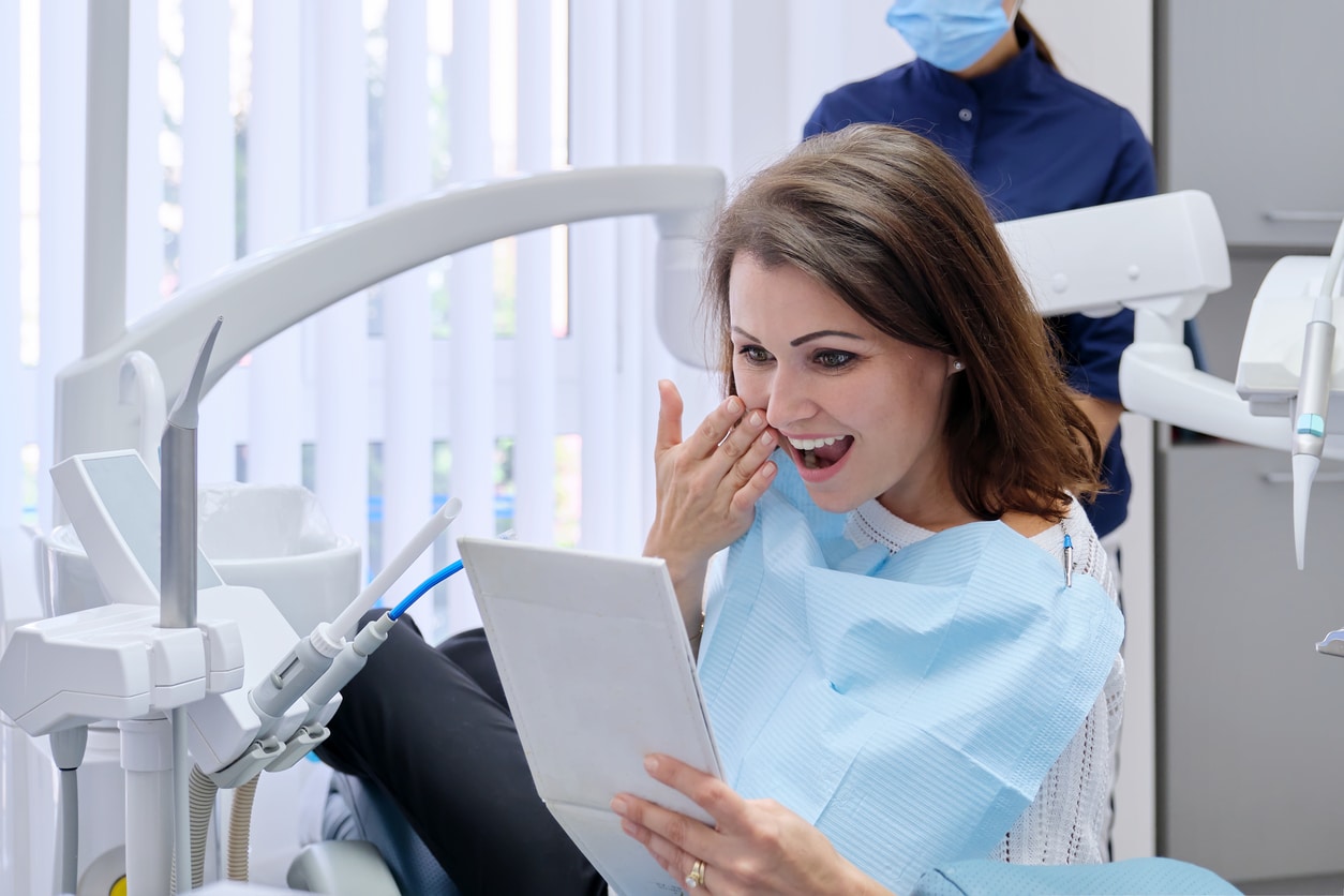 Happy middle aged woman with doctor dentist looking in mirror at teeth