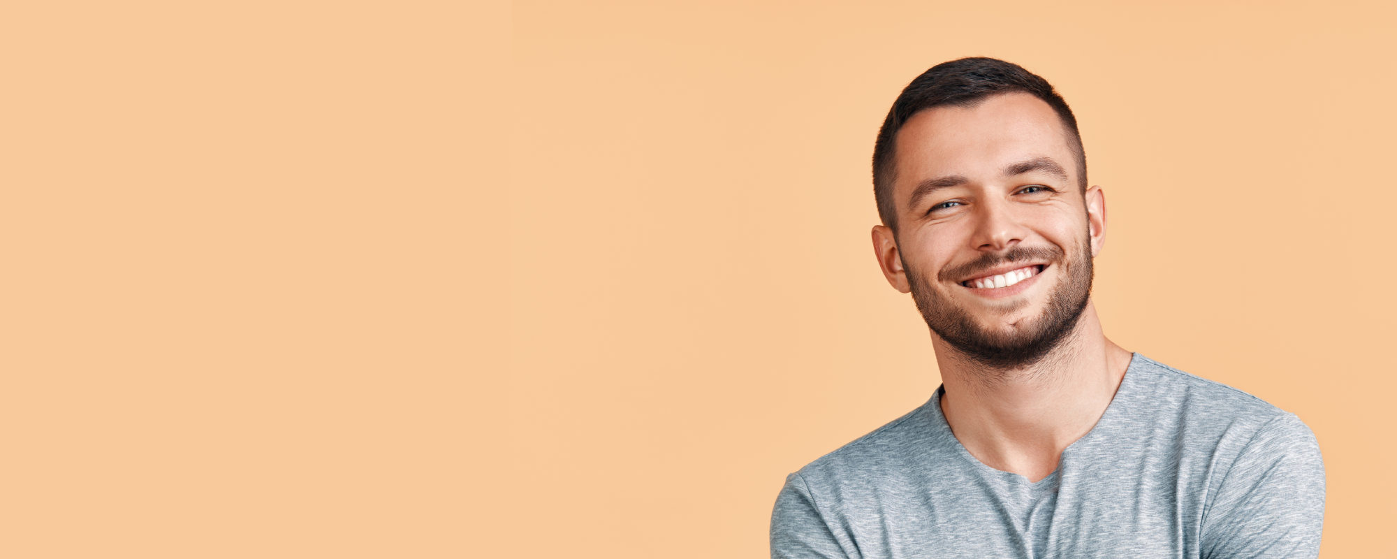 man smiling with grey shirt on on peach background