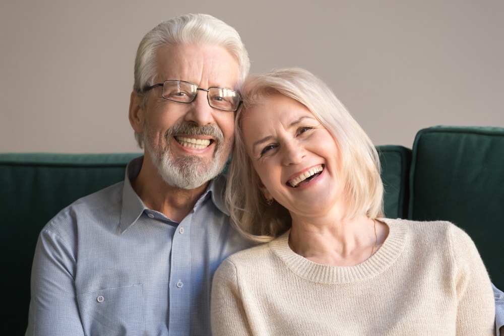 Head shot laughing retirees pretty couple sitting on couch at home