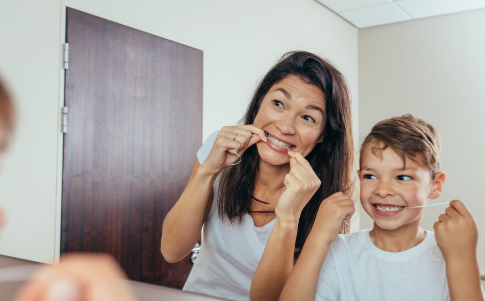 Little boy with his mother in bathroom cleaning teeth with dental floss. Woman with son looking in mirror and cleaning teeth.