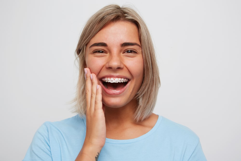 Cheerful beautiful young woman with blonde hair and braces on teeth laughing and touching her face